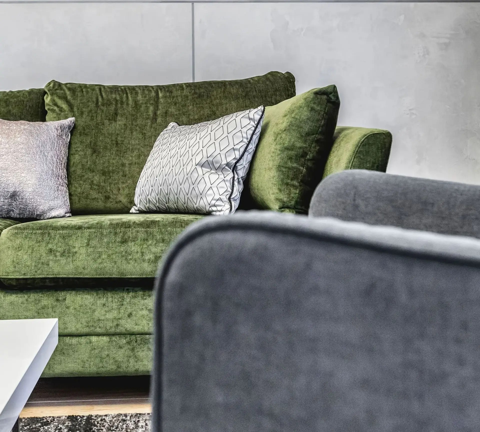 Living met mat-metallic kalkpleister wand in zacht parelgrijs, mosgroene fluwelen bank en antraciet fauteuil
