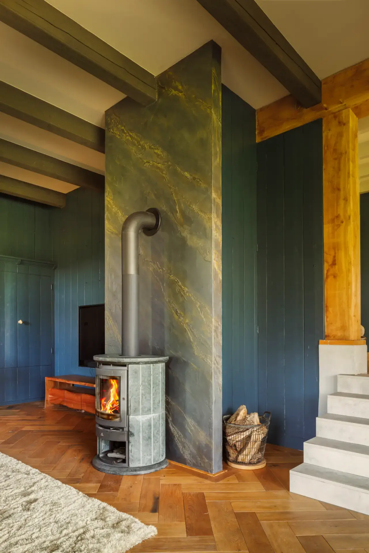 Architectonische context — De haardwand als vrijstaand volume tussen donkerblauwe wandpanelen, eiken spanten en een betonnen trap. Foto: Wouter van der Sar.