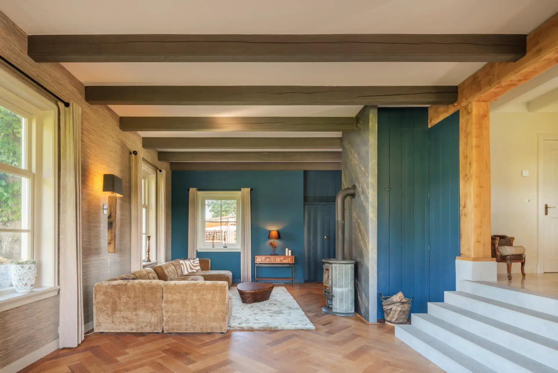 Ruimtelijk overzicht — De haardwand in de volledige woonkamer, tussen balkenplafond, blauwe wanden en eiken portaal. Foto: Wouter van der Sar.